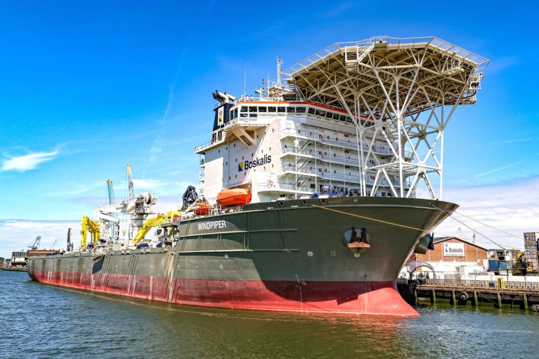 The Boskalis subsea rock installation vessel Windpiper berthed alongside a quay, showing its large cargo capacity and distinctive elevated fall-pipe installation structure above the bow