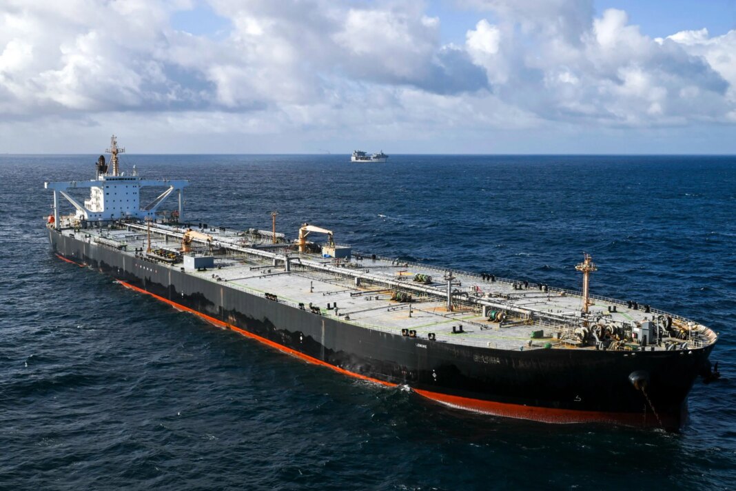 U.S. Revokes Iran Oil Waiver After Hormuz Attacks, Launches New Military Strikes A large crude oil tanker identified as MT Davina sails in open ocean under partly cloudy skies. The black-hulled vessel is viewed from above and ahead, with another ship visible on the horizon in the background.